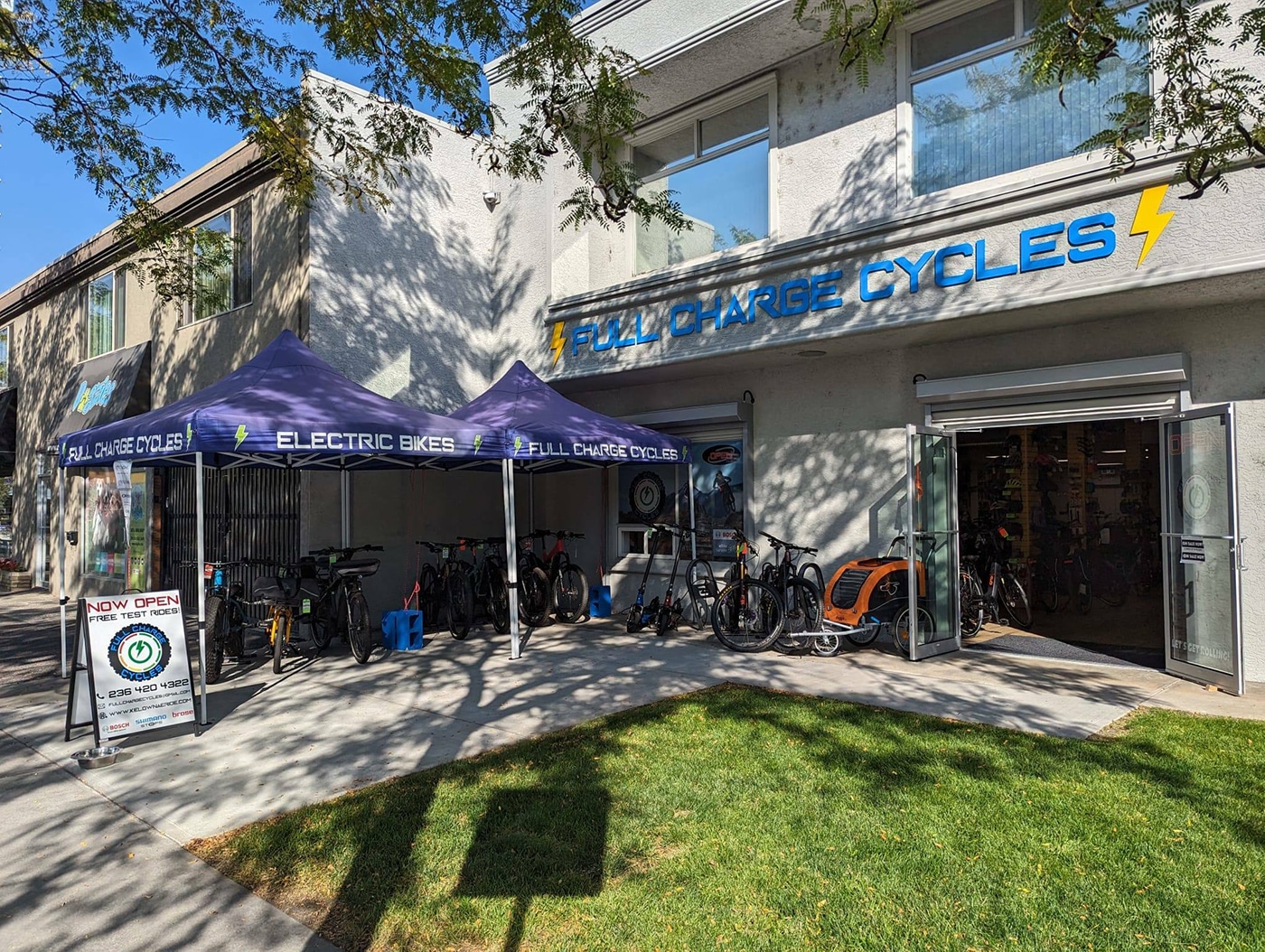 A bike shop named Full Charge Cycles in Kelowna, featuring tents and bicycles displayed on the sidewalk.