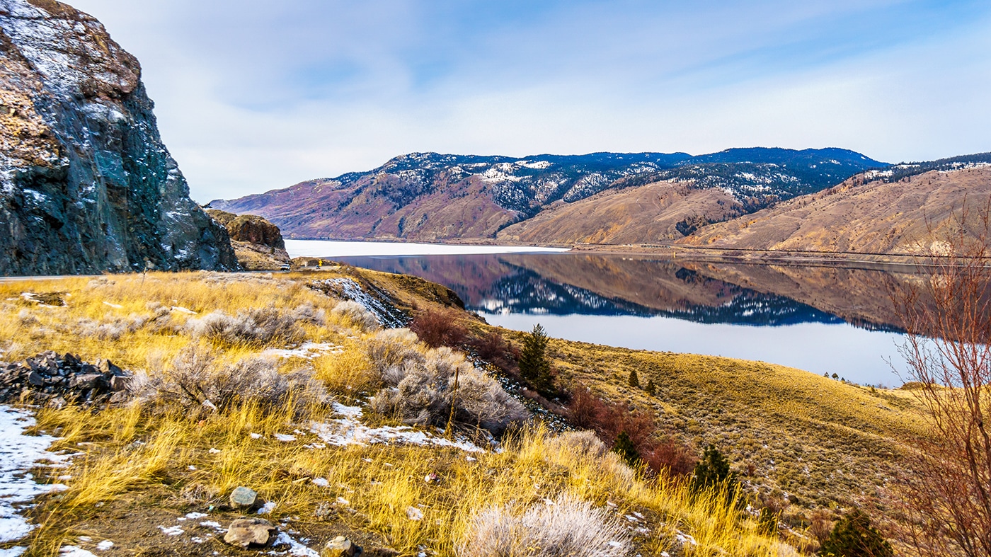 A serene winter view of Mountain River, showcasing a lake surrounded by snow-capped mountains.